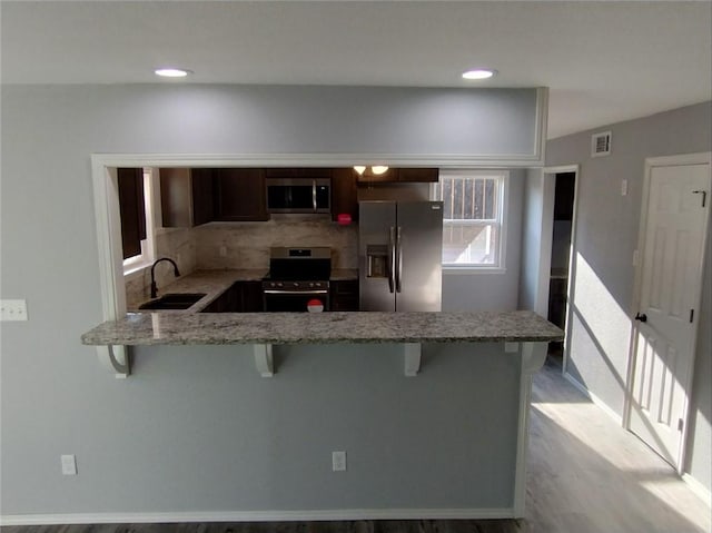 kitchen featuring a breakfast bar, kitchen peninsula, appliances with stainless steel finishes, and light hardwood / wood-style floors