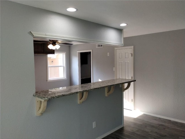 kitchen featuring stone countertops, dark hardwood / wood-style flooring, a kitchen bar, and ceiling fan