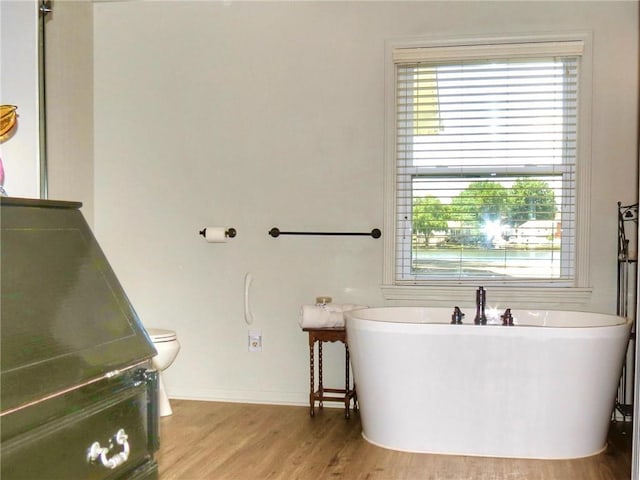 1005 Johnston Dr, Raymore, MO 64083 - bathroom with a soaking tub, toilet, wood finished floors, and baseboards