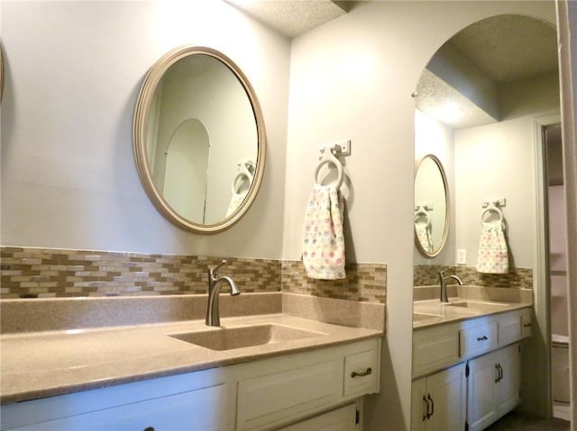 1005 Johnston Dr, Raymore, MO 64083 - bathroom featuring backsplash, two vanities, and a textured ceiling