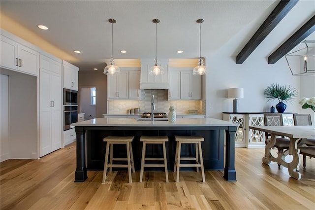 kitchen featuring white cabinetry, hanging light fixtures, a center island with sink, and backsplash