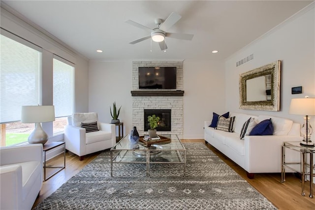 living room featuring crown molding, a brick fireplace, hardwood / wood-style floors, and ceiling fan