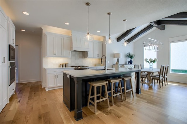 kitchen with hanging light fixtures, sink, a center island with sink, and white cabinets