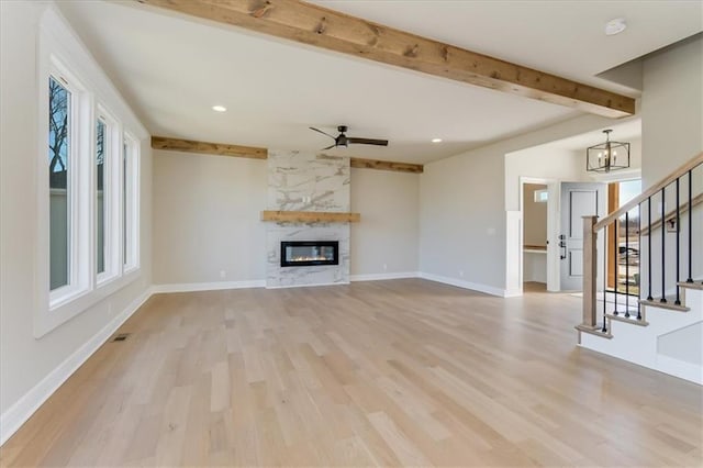 unfurnished living room with stairs, a large fireplace, beam ceiling, and baseboards