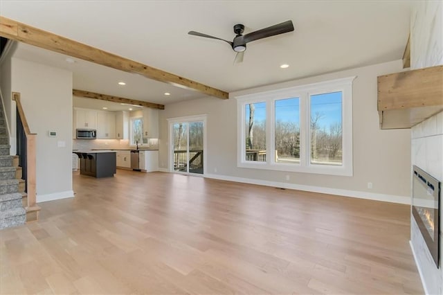 unfurnished living room with baseboards, light wood-style flooring, stairs, a fireplace, and beam ceiling