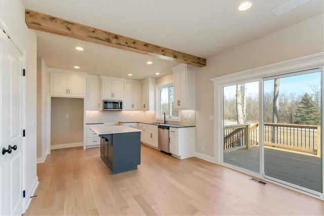 kitchen with tasteful backsplash, visible vents, appliances with stainless steel finishes, a center island, and beam ceiling