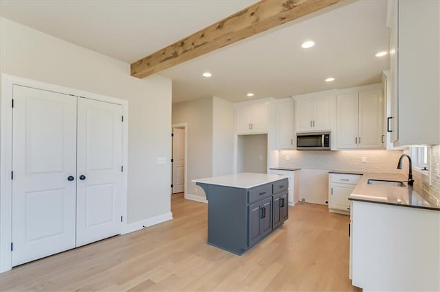 kitchen with white cabinets, light wood-style flooring, stainless steel microwave, beamed ceiling, and a sink