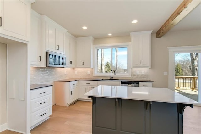 kitchen with light wood-style flooring, a kitchen island, a sink, appliances with stainless steel finishes, and tasteful backsplash