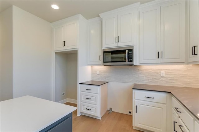 kitchen with recessed lighting, stainless steel microwave, decorative backsplash, white cabinets, and light wood-type flooring