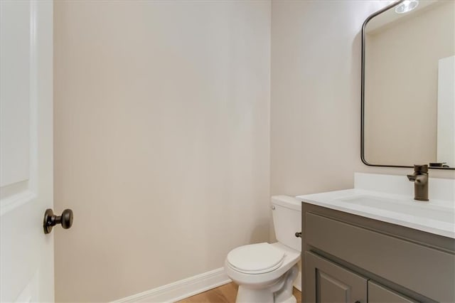 half bathroom with wood finished floors, vanity, toilet, and baseboards