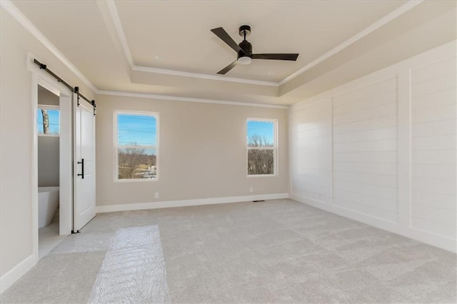 unfurnished room featuring a barn door, a tray ceiling, a wealth of natural light, and ornamental molding