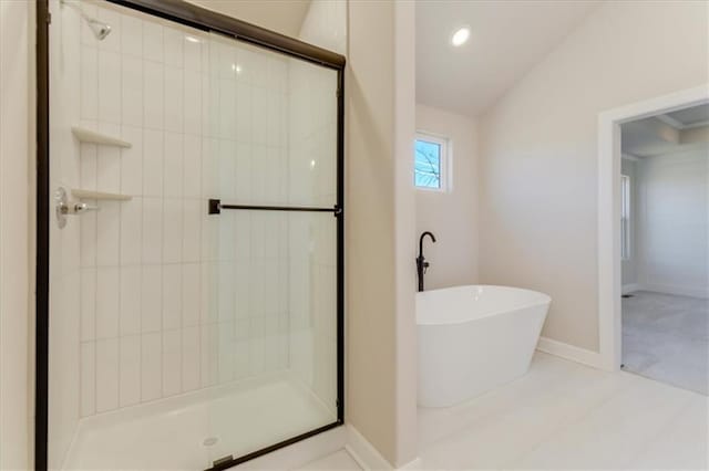 bathroom featuring a soaking tub, a shower stall, baseboards, and vaulted ceiling