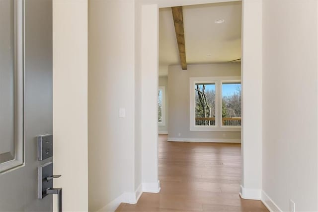 hallway featuring beamed ceiling, baseboards, and wood finished floors