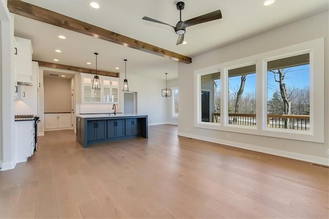 kitchen with a wealth of natural light, beam ceiling, white cabinetry, and wood finished floors