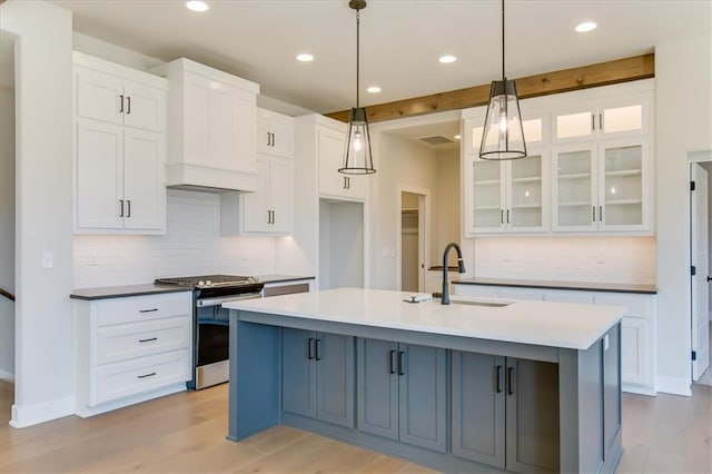 kitchen with a sink, light wood-style flooring, a center island with sink, and stainless steel range with gas stovetop