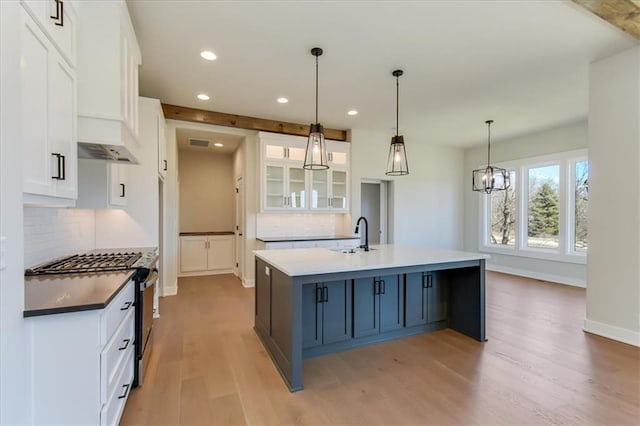 kitchen with light wood-style floors, white cabinetry, an island with sink, and gas range