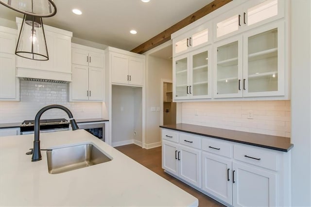 kitchen with decorative light fixtures, a sink, white cabinetry, backsplash, and glass insert cabinets