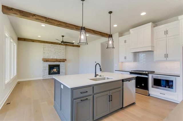 kitchen with decorative backsplash, appliances with stainless steel finishes, gray cabinets, premium range hood, and a sink