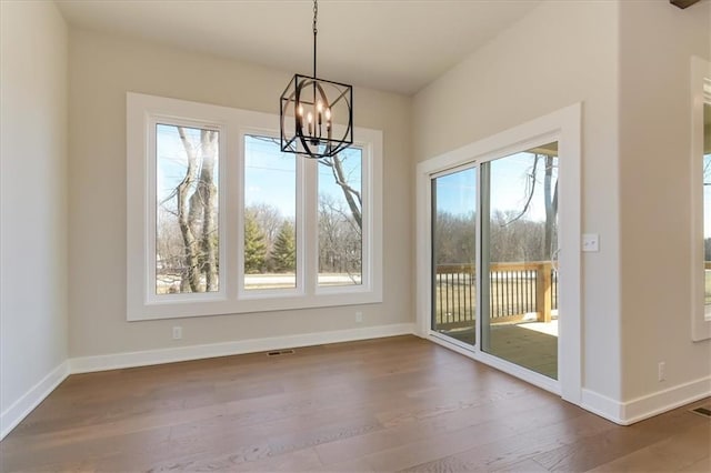 unfurnished dining area featuring a chandelier, wood finished floors, visible vents, and baseboards