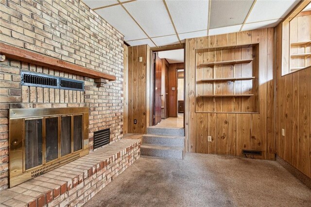 interior space with a drop ceiling, wooden walls, and a fireplace