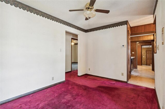 carpeted empty room with ceiling fan and wooden walls