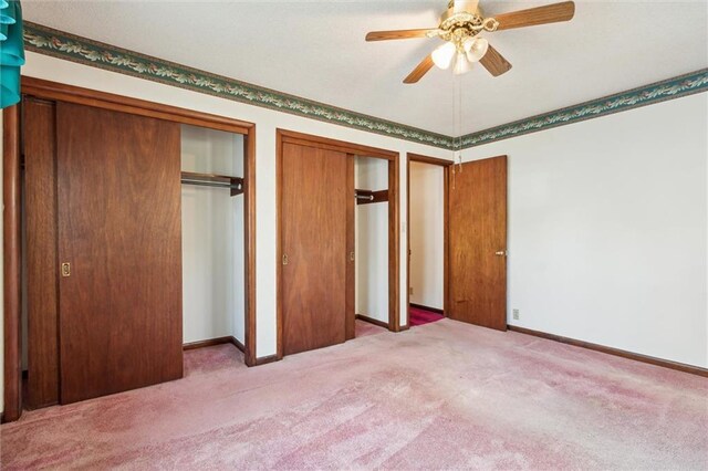 unfurnished bedroom featuring ceiling fan, light colored carpet, and multiple closets