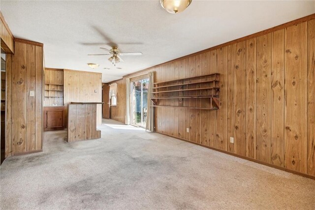 unfurnished living room with ornamental molding, ceiling fan, wood walls, and light carpet