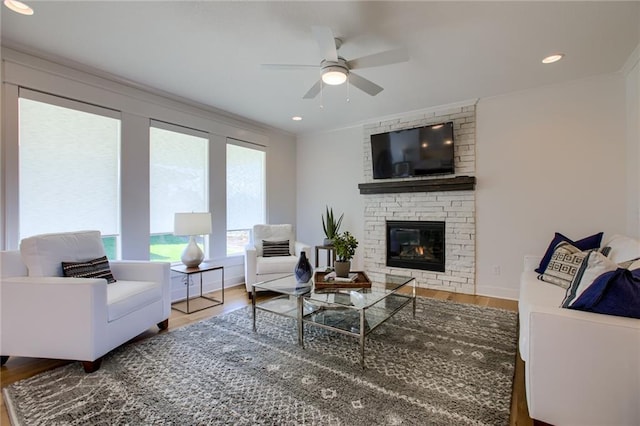 living room with a fireplace, wood-type flooring, ornamental molding, and ceiling fan