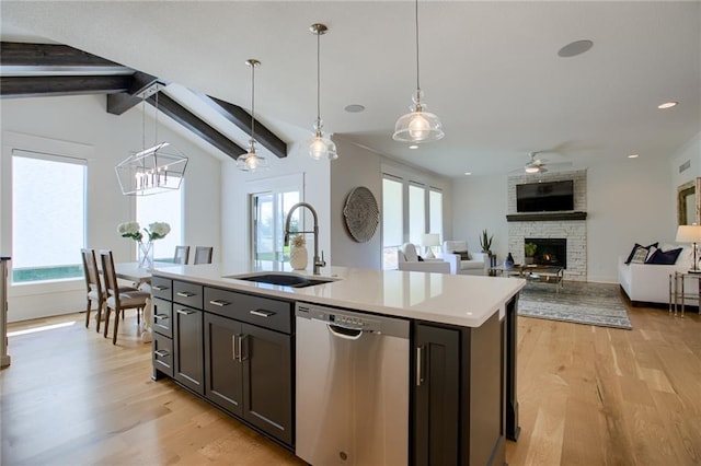 kitchen featuring a stone fireplace, pendant lighting, dishwasher, sink, and a center island with sink