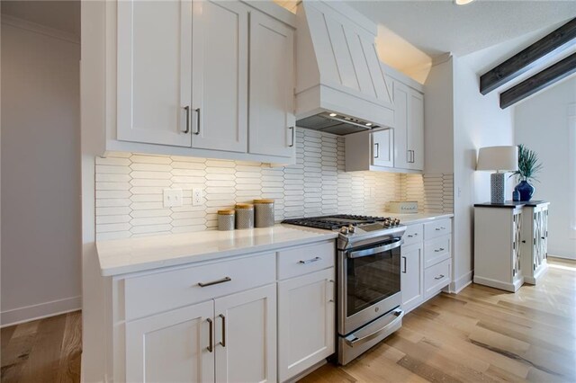 kitchen with stainless steel gas stove, white cabinetry, custom exhaust hood, and light hardwood / wood-style floors