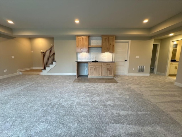 unfurnished living room with a raised ceiling, sink, and light colored carpet