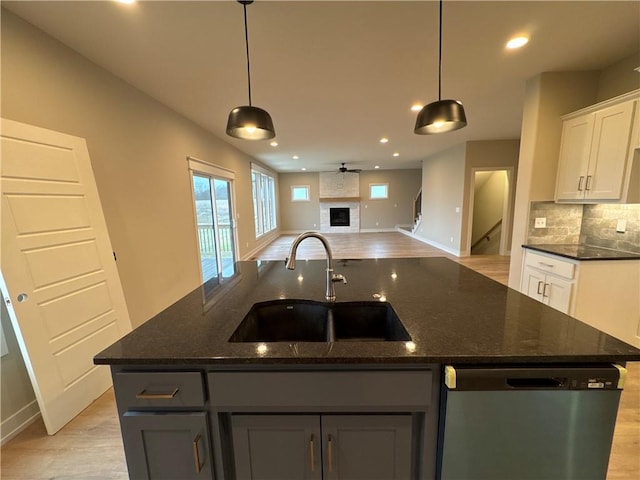 kitchen with white cabinetry, stainless steel dishwasher, an island with sink, and sink