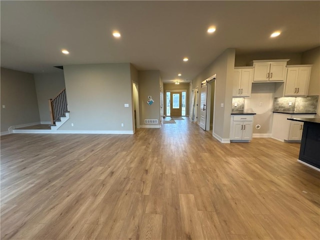 kitchen with decorative backsplash, a barn door, white cabinets, and light wood-type flooring