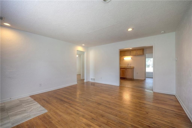 empty room with hardwood / wood-style floors, a textured ceiling, and sink