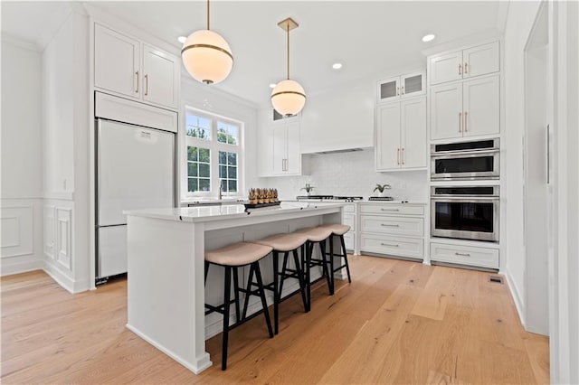 kitchen featuring white cabinetry, a center island, stainless steel double oven, paneled built in refrigerator, and light hardwood / wood-style floors