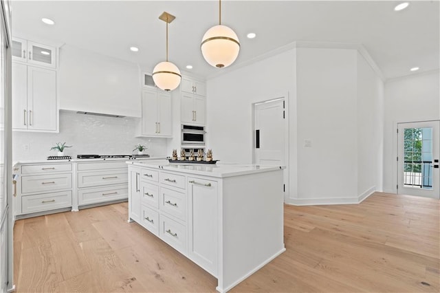 kitchen with pendant lighting, stainless steel oven, white cabinetry, and light hardwood / wood-style flooring