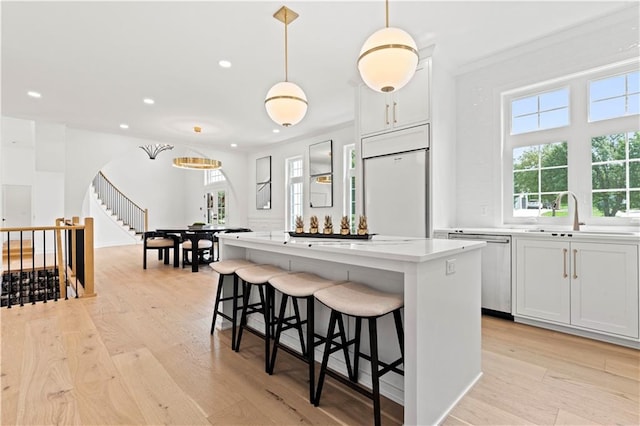 kitchen with paneled fridge, a kitchen island, stainless steel dishwasher, pendant lighting, and white cabinets