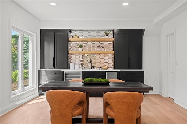 bar with light hardwood / wood-style floors, sink, backsplash, and beverage cooler