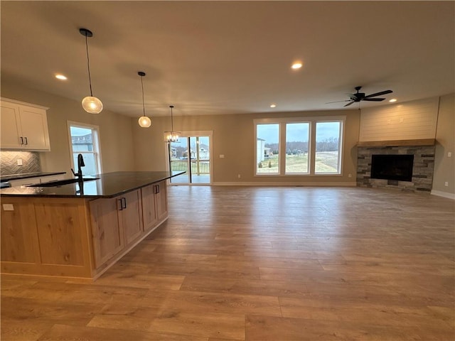 kitchen with sink, white cabinetry, decorative light fixtures, a center island with sink, and light hardwood / wood-style flooring