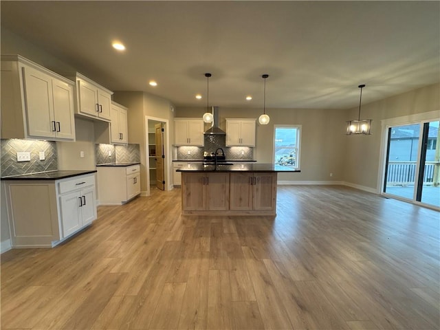 kitchen featuring a kitchen island with sink, decorative light fixtures, wall chimney exhaust hood, and white cabinets