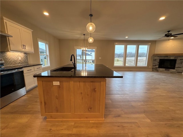 kitchen with pendant lighting, electric stove, a center island with sink, and white cabinets