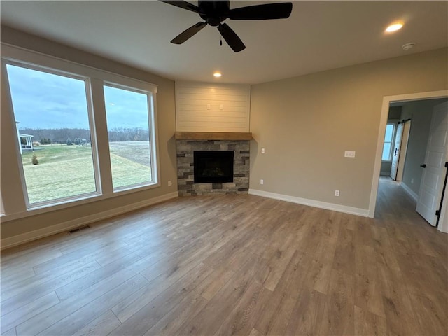 unfurnished living room featuring a stone fireplace, ceiling fan, and light wood-type flooring