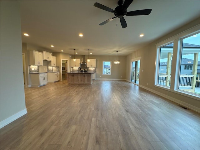 unfurnished living room featuring sink, ceiling fan with notable chandelier, and light wood-type flooring