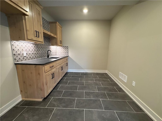 kitchen with dark tile patterned floors, sink, light brown cabinets, and decorative backsplash