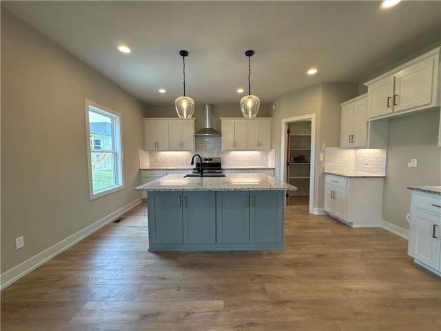 kitchen featuring white cabinetry, an island with sink, and wall chimney exhaust hood