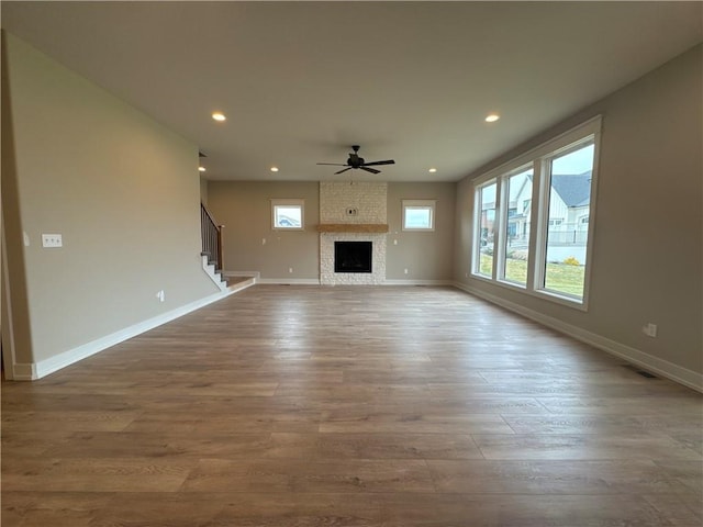 unfurnished living room featuring wood-type flooring, plenty of natural light, ceiling fan, and a fireplace