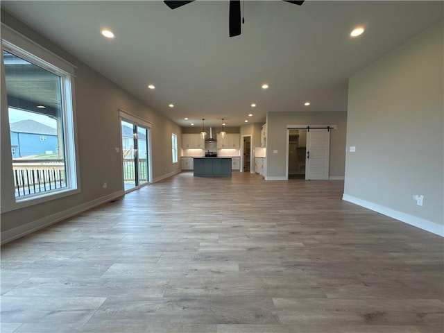 unfurnished living room featuring a barn door, light wood-type flooring, and ceiling fan