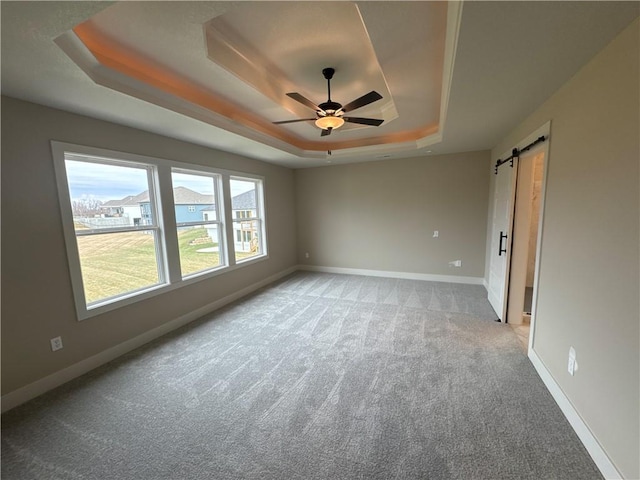 spare room with a barn door, light colored carpet, ceiling fan, and a tray ceiling