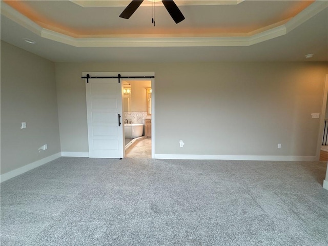 carpeted empty room with ceiling fan, a barn door, and a raised ceiling