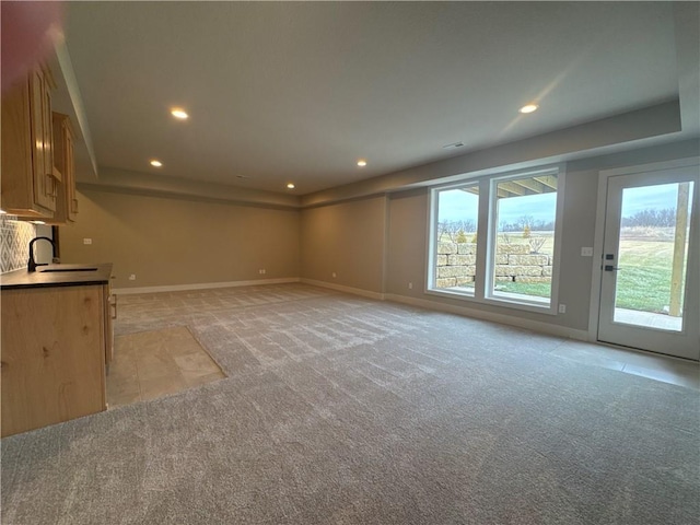 unfurnished living room featuring light carpet, sink, and a healthy amount of sunlight